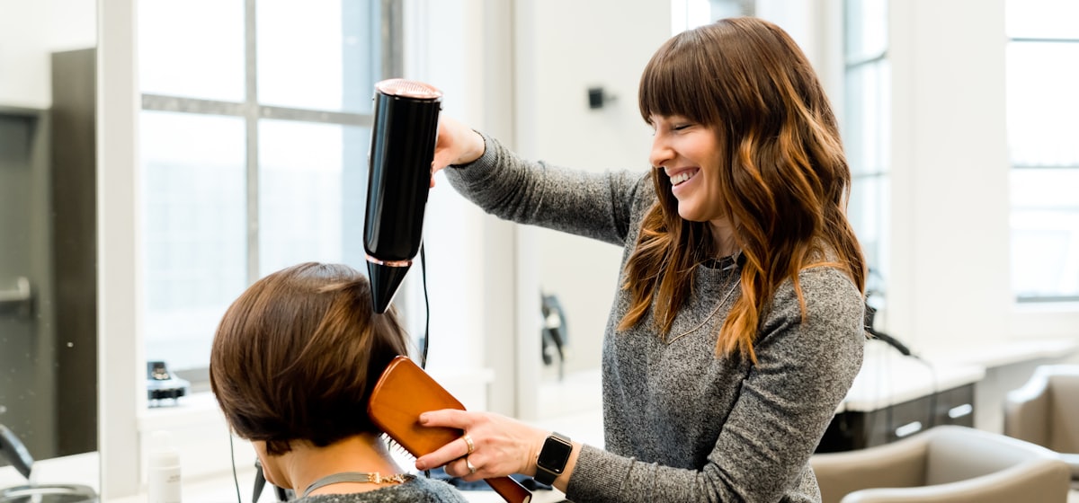 Stylistin föhnt einer Kundin lächelnd die Haare im Föhnfrisch Salon
